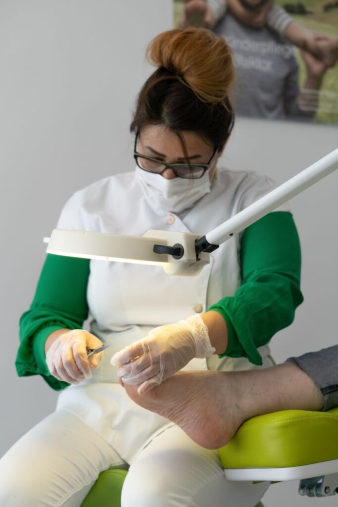 Concentrated skilled specialist wearing medical uniform doing procedure on leg of crop customer under light of lamp